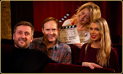 Arek Zasowski with Viola Zasowska, Paul A. Taylor, and Olga Malchevska smiling in a red velvet cinema as they celebrate wrap day for Let Go: Letting Go, holding a clapperboard behind the scenes